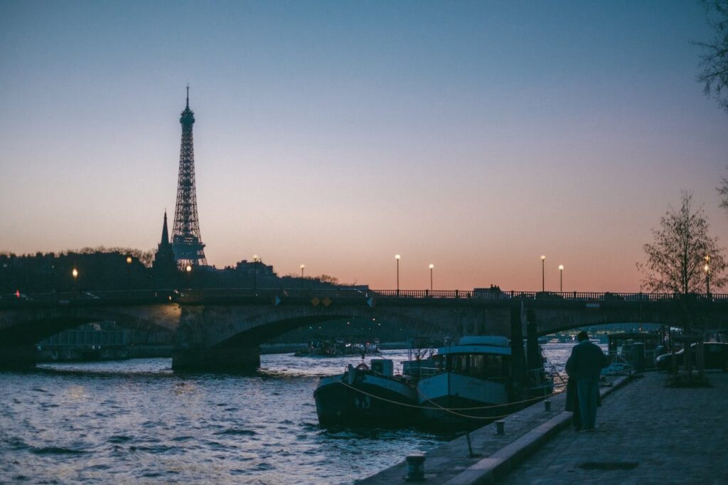 Iconic Eiffel Tower against a serene sunset sky, seen from the Seine River bank in Paris.